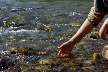 Women's hands, water is pouring near the river. People in nature. Ecology. A woman touches the water with her hands.