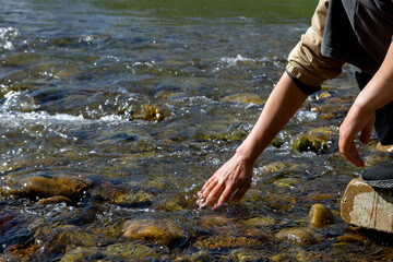 Women's hands, water is pouring near the river. People in nature. Ecology. A woman touches the water with her hands.