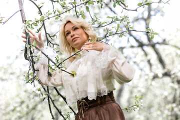 A beautiful girl with blond hair in a white blouse and a long brown retro skirt stands in the...