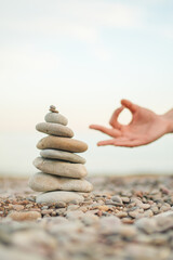 A hand is reaching for a stack of rocks, which are arranged in a pyramid shape. Concept of balance and harmony, as the hand is reaching for the rocks in a peaceful and serene manner