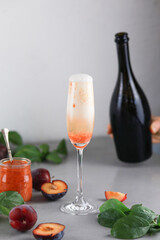Bellini plums champagne cocktail in crystal glass and fresh fruits on gray table.