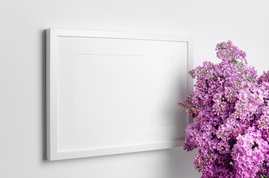 Blank landscape picture frame mockup on whte wall with fresh lilac flowers bouquet