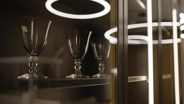 Wine glasses in a wooden cabinet, a shelf behind glass, beautiful white lighting. Beautiful wine glasses in a cabinet in the interior.
