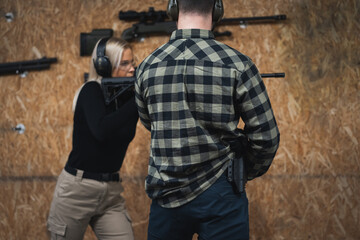 Fototapeta premium A young girl learns to shoot a tactical rifle at a shooting range with an instructor.