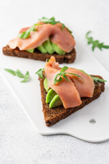 Sandwich with avocado, salmon and grain bread close-up view on white background
