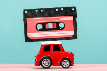 Little red car carrying cassette tape on roof on blue and pink background. Road trip songs concept.