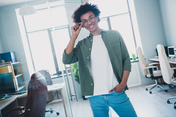 Photo of cheerful handsome agent dressed khaki shirt arm hand eyewear smiling indoors workshop...