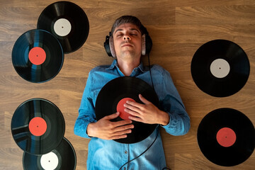 Top view man music lover with headphones lie on the floor and listen music among retro vinyl records