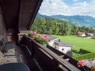 View from wooden balcony with geranium flowers, table and chairs in the village of Wiesing towards green valley with Alps and Lake Achensee in Tyrol, Austria. Summer sunny day.