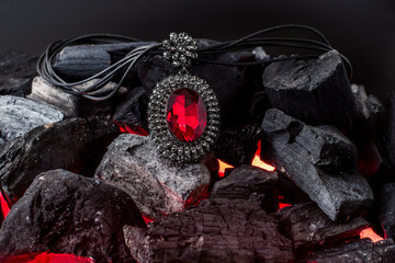 red stone pendant with diamonds around it lies on burning coals
