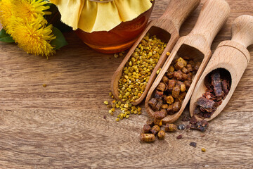 A jar of honey with fabric lid, pollen granules, beebread, and dandelion flowers