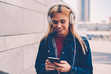 Smiling young woman in denim wear choosing music on internet website to download in playlist on...