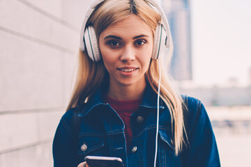 Half length portrait of attractive blonde student looking at camera while listening audio lesson of...