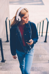 Stylish young woman in modern white headphones listening electronic music downloaded on own...