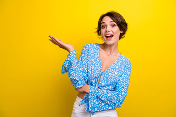 Photo of excited funky young lady dressed flower print top showing arm empty space isolated yellow color background