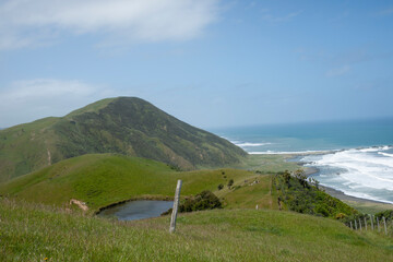 Hilly farmland with pond and view down to coast and surf under blue sky