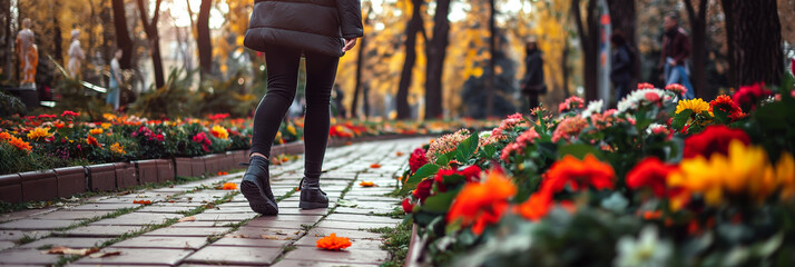 Side view of a pedestrian in chic clothing walking past colorful flowerbeds in a park 