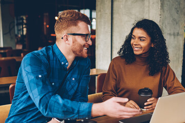 Smiling male teacher with red hair explaining new topic for study to cheerful african american...