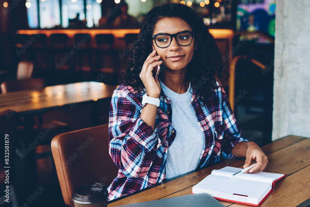 Poster african american student in stylish eyeglasses talking with mobile operator on smartphone while crea
