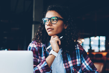 Thoughtful african american young woman with curly hair thinking on creative ideas for writing...