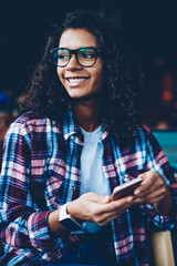 Beautiful african american hipster girl in eyeglasses smiling while sending sms message to friend...