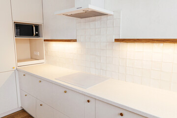 Modern minimal kitchen design. Stylish white electric cooker, kitchen cabinets with brass knobs, granite counter, wooden shelves and appliances in new scandinavian house.  Modern kitchen interior