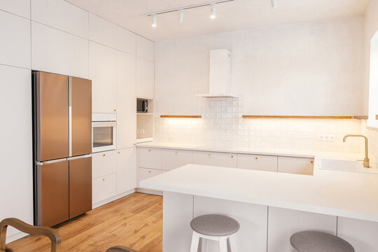 Modern minimal kitchen design. Modern kitchen interior. Stylish white kitchen cabinets with brass knobs, faucet, granite island and appliances in new scandinavian house.