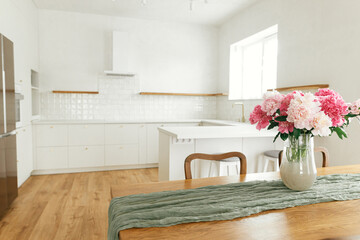 Beautiful peonies in vase on wooden table on background of stylish white kitchen with appliances in...