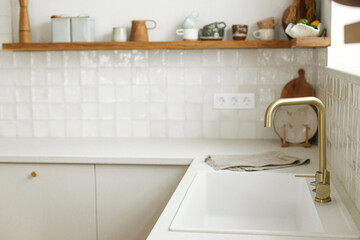 Modern kitchen interior. Stylish white kitchen cabinets, brass faucet and granite sink, wooden...