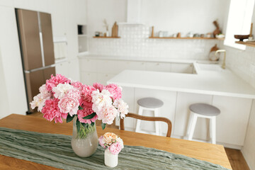 Modern kitchen interior. Beautiful peonies in vase on wooden table on background of stylish white kitchen with appliances in new scandinavian house.Summer floral arrangement