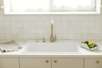 Fototapeta premium Limes in bowl and brass faucet on background of modern white kitchen with granite countertop and towel in new scandinavian house. Modern kitchen interior