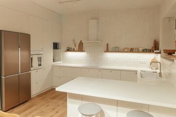 Modern kitchen interior. Stylish white kitchen cabinets with brass knobs, granite island, appliances and evening light in new scandinavian house. Modern minimal kitchen design