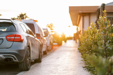 Row of cars parked near the sunny sidewalk in front of the house