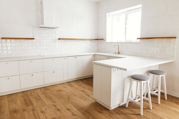 Modern minimal kitchen design. Modern kitchen interior. Stylish white kitchen cabinets with brass knobs, faucet, granite island, wooden shelves and appliances in new scandinavian house.
