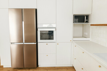 Modern kitchen interior. Stylish white kitchen cabinets with brass knobs, granite counter and...