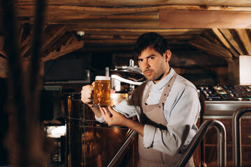 Young man examining the quality of craft beer at brewery. Male inspector working at alcohol manufacturing factory checking the beer.