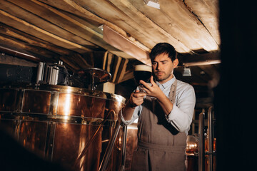 Young man examining the quality of craft beer at brewery. Male inspector working at alcohol manufacturing factory checking the beer.