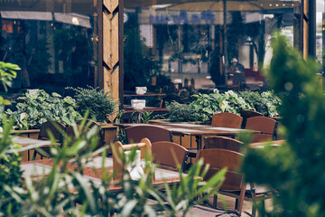 Early in the morning, there are wooden tables and chairs on the terrace of the outdoor summer cafe. Selective focus on tropical green plants with space to copy. High quality photo