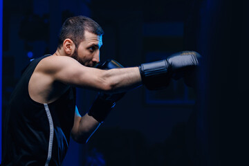 Male boxer trains punches on punching bag, dark background. Concept banner sport boxing