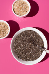 Semillas de chía y semillas de sésamo en un bol blanco sobre fondo rosa. Vista superior