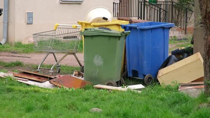 Old Discarded Household Furniture Dumped by Colorful Plastic Dumpsters for Bulk Item Pickup by City Cleaning Services