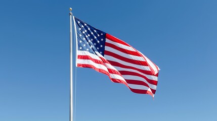 Fototapeta premium The photo shows an American flag waving in the wind. The flag is blowing to the right. The sky is clear and blue.