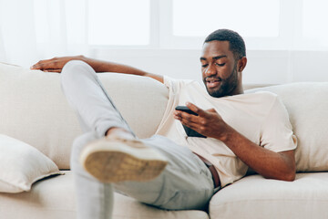 Happy African American man sitting on a black sofa, using his mobile phone The modern apartment...
