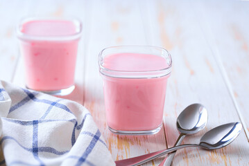 Two portions of homemade strawberry yogurt in a glass jars on a white table, selective focus.