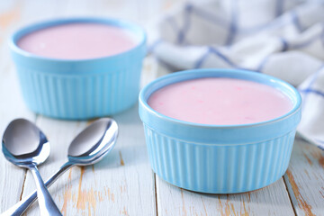 pink fruit yogurt in a ceramic bowl with spoon on a light background, selective focus.