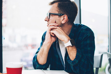 Young creative male blogger dressed in trendy clothes looking at window and pondering about good...