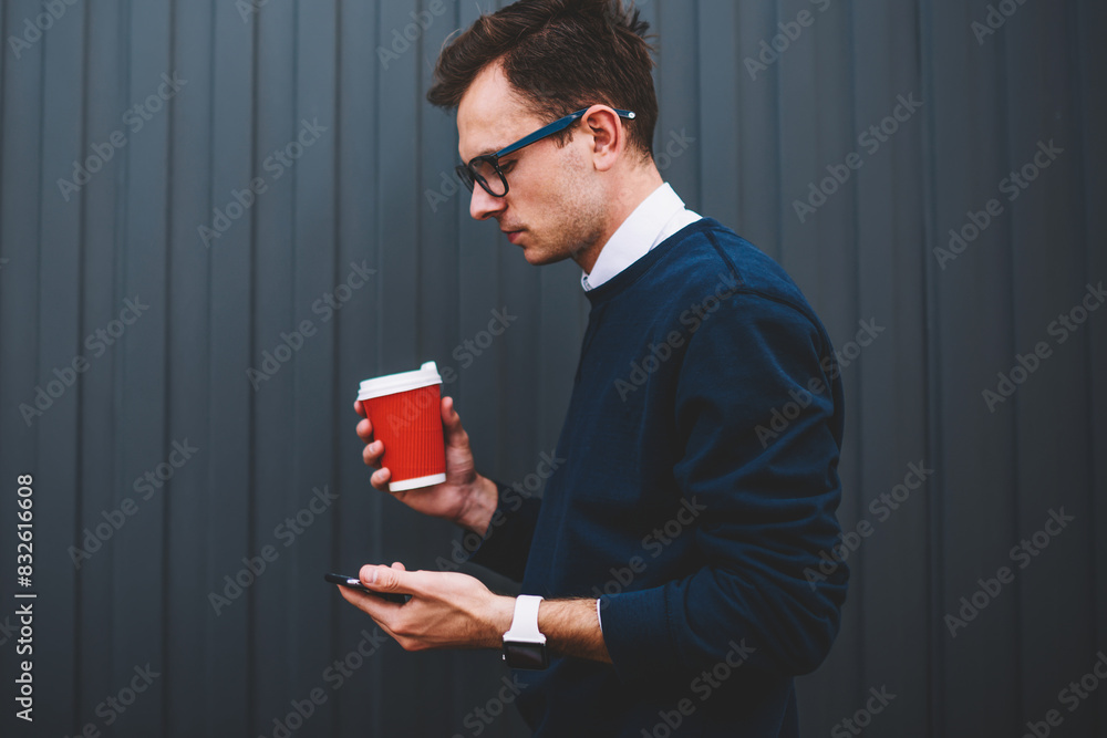 Poster pensive male blogger in trendy eyeglasses checking email message using smartphone application during