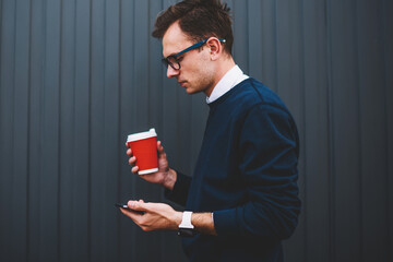 Pensive male blogger in trendy eyeglasses checking email message using smartphone application...