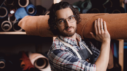 Portrait man tailor industry, craftsman on background different rolls natural brown leather, warm...