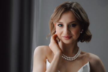 Portrait of happy elegant young woman in modern bridal look with classic hairstyle and makeup with pearl necklace